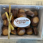 A top-down view of a white gift box filled with chocolate-covered caramel candies, tied with a gold ribbon and featuring a white label that reads 'Chocolate Corner'.